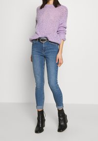 Suéter de punto morado con un corte holgado, combinado con jeans skinny azules. Botines de tacón negro y un cinturón plateado con adornos.