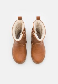 Botas de cuero marrón hasta el tobillo con un suave forro de piel de color crema y cierre de cremallera. Presentan una lengüeta en el talón. Textura suave, punta redondeada.