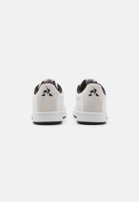 Baskets blanches et grises avec des accents en daim, cuir lisse, bout rond, semelles en caoutchouc blanches et un logo sur le talon.