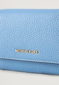 Sinine tekstuurne nahast rahakott kuldse "MICHAEL KORS" logoga. Omab õmbluse detaile ja klappkinnitust. Kompaktne disain, sobib kaartide jaoks.