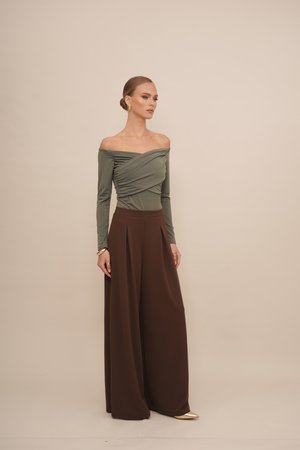 Olivegrünes Off-Shoulder-Oberteil mit geraffter Textur, kombiniert mit weiten, plissierten braunen Hosen und goldenem Schuhwerk. Glatte Stoffoberfläche.