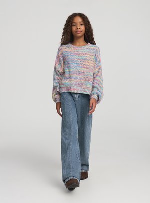 Maglione lavorato a maglia multicolore con design testurizzato, vestibilità ampia e polsini a costine abbinato a jeans larghi azzurri e scarpe marroni.