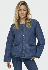 Jakna od denim tkanine s modelom romb, tamnoplave boje, kojoj je karakterističan okrugli izrez, prednje kopčanje na dugmad i dva bočna džepa. Glatka tekstura i opušteni kroj.