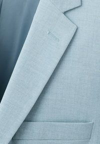 Lyseblå skræddersyet jakkesætjakke med revers, knaphul og en brystlomme på en tekstureret stofbaggrund.