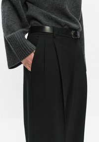 Czarne dopasowane spodnie z plisami z przodu, wysoki stan i gładka tekstura, zestawione z ciemnoszarym swetrem z prążkowanej tkaniny oraz czarnym paskiem.