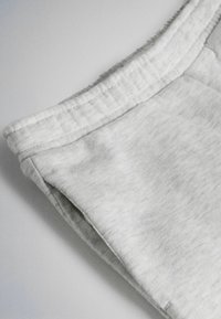 Lichtgrijze stoffen tailleband met zichtbare stikdetails en een zijnaadzak op een zacht kledingstuk.