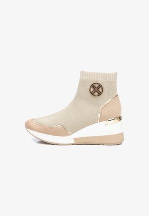 Beżowy dziergany botek za kostkę na koturnie, zamszowe akcenty na czubku i pięcie, elastyczny mankiet oraz dekoracyjna, okrągła metalowa naszywka z boku.