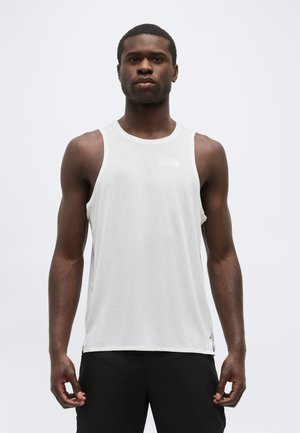 Urheilullinen mies, jolla on valkoinen hihaton verkkoliivi ja mustat shortsit, seisoo yksinkertaista valkoista taustaa vasten.