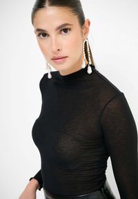 Top nero a maniche lunghe in tessuto trasparente con colletto alto; presenta un design aderente, una texture liscia e orecchini a perla pendenti in strati.