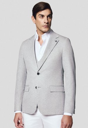 Szary blazer z miękkiego materiału o dopasowanym kroju, z dwiema kieszeniami, zapięciem na jeden guzik, klapami oraz kontrastową białą koszulą pod spodem.