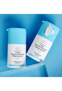 Drunk Elephant F-Balm Electrolyte Waterfacial Masque. Two cylindrical bottles, light blue tops, white bodies, with labels and cream texture visible.
