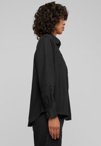 Black button-up shirt made of lightweight fabric, featuring a classic collar, long sleeves, and a relaxed fit with a curved hem.