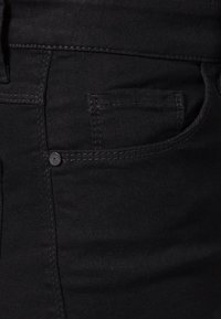 Jean en denim noir avec un design classique à cinq poches, des coutures contrastées et une taille standard avec fermeture à bouton.