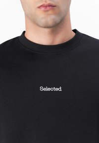 Black cotton t-shirt with a crew neckline and white "Selected" embroidery on the chest. Features a smooth texture and classic design.