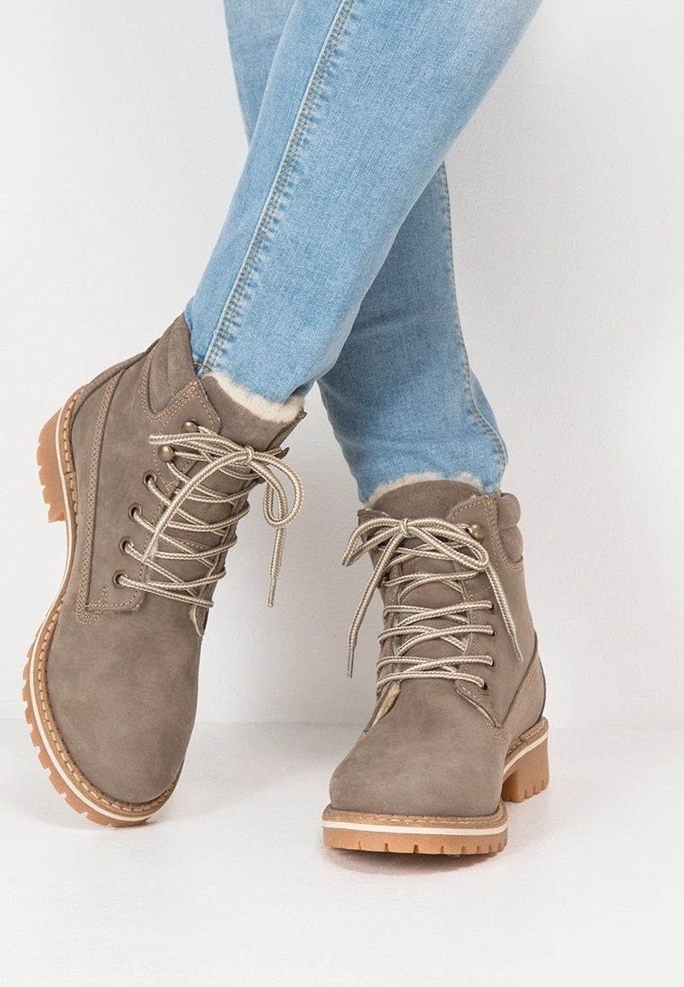 Bottes d'hiver marron clair à lacets avec doublure en fourrure portées avec un jean skinny bleu clair, posées sur un fond blanc.