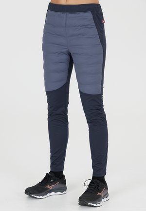 Pantalons de sport rembourrés combinant des matériaux gris clair et bleu marine foncé. Présente un design ajusté, une taille élastique et des poches zippées sur les côtés.