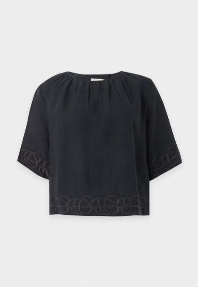 Blouse noire ample à manches courtes avec col rond et broderie subtile en boucles le long de l’ourlet et des bords des manches sur fond uni.