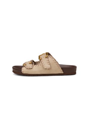Beige Wildleder-Pantoletten mit zwei verstellbaren goldfarbenen Schnallen und brauner flacher Sohle, mit abgesteppten Details entlang der Ränder.
