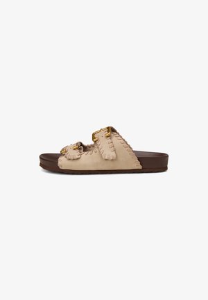 Beige Wildleder-Pantoletten mit zwei verstellbaren goldfarbenen Schnallen und brauner flacher Sohle, mit abgesteppten Details entlang der Ränder.