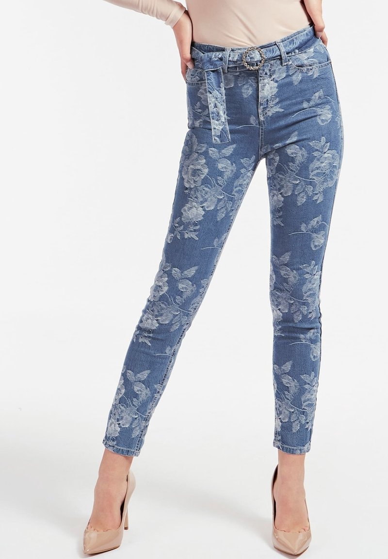 Jeans de mezclilla con estampado floral en azul claro, que presentan un diseño ajustado, detalle de cinturón y una textura suave, combinados con tacones nude.