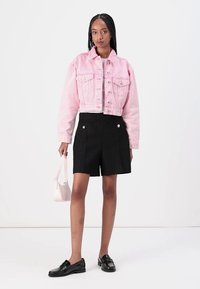 Vaaleanpunainen lyhyt denim-takki, mustat räätälöidyt shortsit, mustat loafers-kengät ja pieni valkoinen käsilaukku. Kangasrakenteet ja napitus näkyvissä.