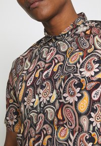 Kortärmad skjorta med paisleymönster i livfulla färger på svart bakgrund, med knäppt krage och strukturerat tyg.