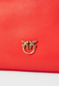 Red leather bag featuring a gold-tone clasp with two bird motifs, showcasing a smooth texture and sleek rectangular design.