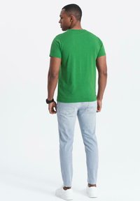 Grön t-shirt med kort ärm, av bomull, med rundad halsringning, ihop med ljusblå slim-fit jeans och vita sneakers. Bakvy visas.