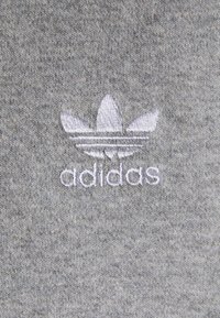 Tejido de sudadera gris con una textura suave que presenta un logo de Adidas bordado en blanco y un diseño de trébol.