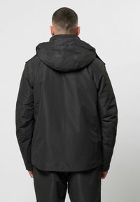 Schwarze wasserdichte Jacke mit Kapuze, die über eine glatte Textur, eine lässige Passform und ein einfaches Design verfügt. Keine sichtbaren Logos oder Muster.