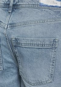 Jeans de denim azul claro con costuras visibles y dos bolsillos traseros. La tela tiene una textura ligeramente desvaída. La etiqueta dice "Street One Loves Denim."