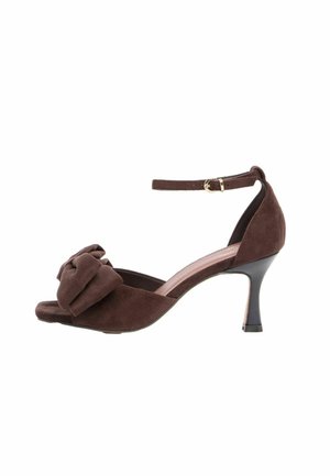 Sandale à talon haut en daim marron avec bout ouvert, bride à la cheville et nœud décoratif à l'avant, présentée sur fond blanc.