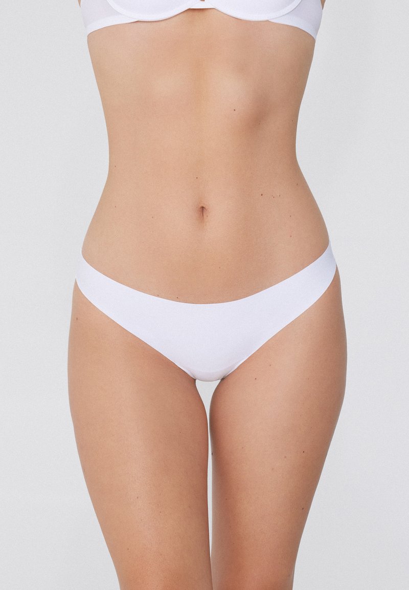 Un string blanc, fabriqué en matériau lisse et extensible, présente un design minimaliste avec une taille basse et des bords sans coutures.