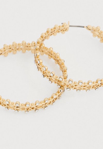 Zlaté náušnice kruhy s prepracovaným vyrezávaným dizajnom, ozdobené drobnými korálkami a priehľadnými drahokamami, ktoré demonštrujú elegantnú textúru a tvar.