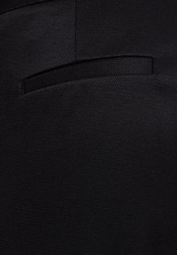 Černá texturovaná látka s viditelným šitím a obrysem rovné kapsy. Povrch vypadá odolně s tkaným vzorem.