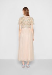 Abito lungo di un tenue rosa pallido con un busto ricamato floreale e maniche a sbuffo trasparenti. Gonna in tulle fluido con una texture a pois e chiusura con zip sul retro.