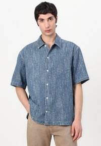 Camicia di jeans a maniche corte con un motivo blu a macchie, chiusura a bottoni e colletto classico. Tessuto texturizzato, vestibilità comoda.