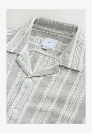 Chemise rayée grise et blanche avec un tissu texturé, dotée d'un col classique, d'une fermeture à boutons et d'une étiquette.