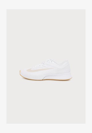 Chaussure de sport basse blanche avec un swoosh Nike beige, tige en mesh et semelle extérieure en caoutchouc marron clair, vue de côté sur fond uni.