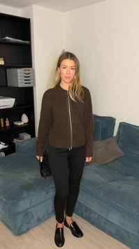 Brown, fuzzy cardigan with a silver zipper, paired with black slim pants and shiny black loafers. Seating area has teal textured upholstery.