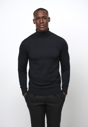 Schwarzer Rollkragenpullover mit glatter Textur, tailliertem Schnitt und gerippten Bündchen, kombiniert mit dunklen, maßgeschneiderten Hosen.