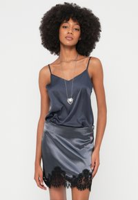 Tengerészkék szatén camisole vékony pántokkal, hozzáillő szatén szoknyával, amelynek szegélyén fekete csipke díszítés található. Az anyag egészében sima textúrájú.