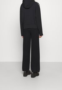 Ensemble sweat à capuche noir et pantalon large, fabriqué en tissu doux. Comprend une capuche, des accents de logo sur l'épaule et des chaussures noires imposantes.