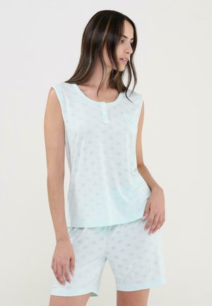 Mujer con top sin mangas azul claro y pantalones cortos a juego con un sutil patrón de estrellas, de pie y mirando hacia un lado.