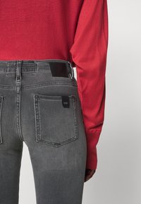 Jeans grises de corte ajustado con bolsillos traseros, una etiqueta de cuero negro en la cintura, combinados con una camiseta de manga larga roja. Material de mezcla de algodón.