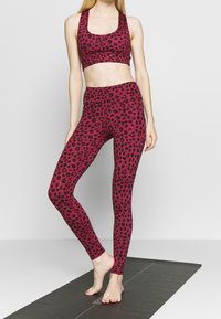 Sada sportovního oblečení s leopardím potiskem v barvách fuchsie a černé, obsahující přiléhavý sportovní podprsenku s širokými ramínky a legíny s vysokým pasem. Hladká struktura látky.