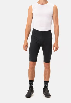 Shorts da ciclismo neri con un design elegante, tessuto elasticizzato e seduta imbottita. Abbinati a una maglietta bianca senza maniche e scarpe da ciclismo nere.