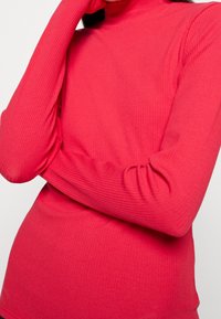 Ribbet, langærmet lyserød turtleneck-top med en tætsiddende pasform. Stoffet er strækbart og struktureret, hvilket fremhæver kroppeformen.