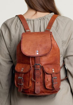 Bruine leren rugzak met flap sluiting, twee voorzakken, zilveren hardware accenten en verstelbare gevoerde schouderbanden. Getextureerd oppervlak.