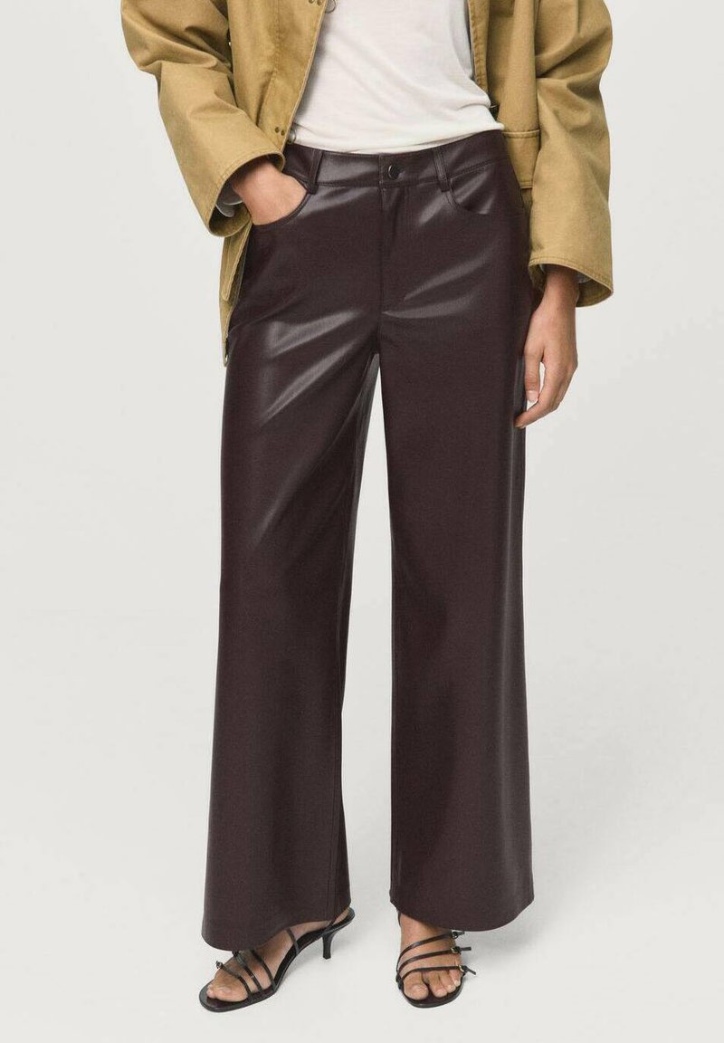 Brown faux leather wide-leg trousers with a glossy finish, featuring a button closure and two front pockets, styled with a beige oversized jacket.
